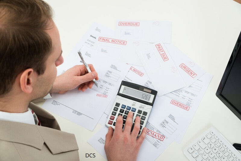 Image of male sat at desk with many invoices and a calculator